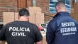 Agentes de costas, de frente para caixas de papelão. Em suas camisetas, está escrito Polícia Civil e Receita Estadual