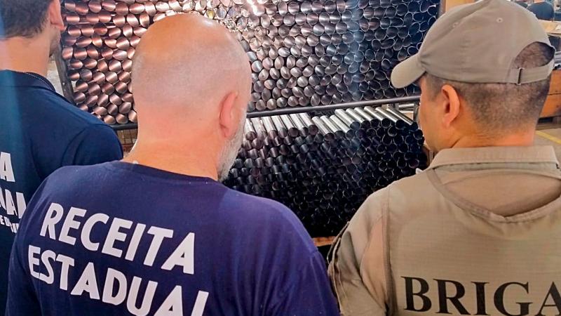 De costas, est&atilde;o dois profissionais com camiseta azul marinho escrito Receita Estadual e um com o uniforme da Brigada Militar.