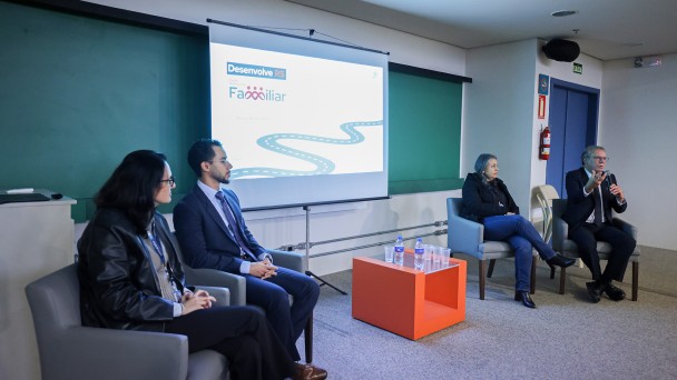 Uma imagem em plano m&eacute;dio e &acirc;ngulo normal mostra quatro palestrantes sentados em poltronas durante um evento institucional em um audit&oacute;rio ou sala de confer&ecirc;ncias.