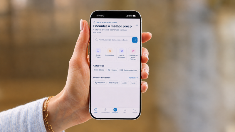 Imagem mostra uma m&atilde;o segurando um celular. Na tela, est&aacute; o layout do aplicativo Menor Pre&ccedil;o Nota Ga&uacute;cha. 